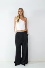 Pantalón de vestir negro de tiro alto con pliegues frontales, corte amplio y pernera recta. Cuenta con bolsillos laterales y cierre frontal con cremallera y botón.