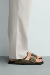 Sandalias de piel con acabado en gamuza, color gris, de diseño plano con plantilla anatómica. Cuenta con dos tiras anchas en el empeine ajustables mediante hebillas metálicas.