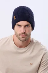 Gorro tejido de punto acanalado en color azul marino, con vuelta y etiqueta decorativa de cuero sintético en el lateral.