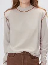 Polera de manga larga confeccionada en tela rib color beige, con cuello alto y hombreras. Presenta costuras decorativas con pespuntes en color contrastante en el cuello, sisas y puños.