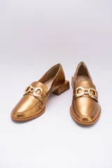 Mocasines de cuero en tono bronce metalizado, con detalle de aplique metálico dorado en el empeine y taco cuadrado bajo de madera.