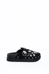 Zueco negro de estilo slip-on, confeccionado con acabado similar a gamuza, suela gruesa dentada de goma, hebilla lateral plateada de diseño occidental y apliques metálicos decorativos con tachas y ojetes en la capellada.
