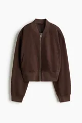 Campera bomber color marrón oscuro de tejido grueso, con cuello corto, puños y bajo acanalados. Cuenta con cierre frontal plateado, bolsillos frontales insertados y diseño de hombros caídos. Está completamente forrada.