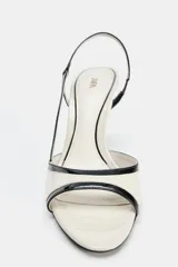 Sandalia de tacón alto fino color blanco marfil con detalles en negro acharolado, diseño destalonado con tira elástica trasera y punta redonda.