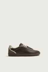 Zapatilla deportiva de estilo retro, confeccionada en una combinación de piezas de cuero texturizado y gamuza en tonos marrones. Presenta un diseño de doble cordonera con cordones claros y suela de goma a tono.