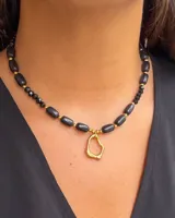 Collar de piedras negras alargadas y cristales checos facetados, con dije colgante de acero quirúrgico de forma orgánica irregular en tono dorado.