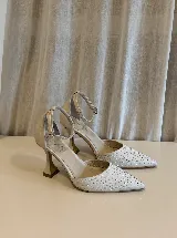 Zapato de tacón con punta fina, confeccionado en tela con aplicación de strass en la capellada y detalles en cuero en el talón, taco y pulsera. Cuenta con cierre de hebilla al tobillo y taco de altura media.