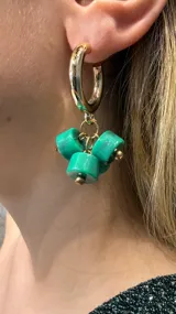 Caravana tipo argolla dorada con tres dijes colgantes de resina en color verde esmeralda con forma cilíndrica.