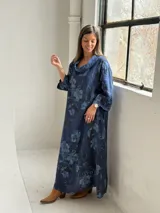 Vestido largo de lino azul marino con estampado floral en tonos más claros, de corte amplio, con cuello tipo cowl y mangas largas.