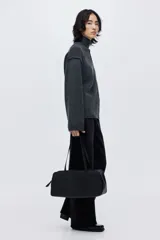 Buzo oversized de punto suave, color gris oscuro, con cuello alto acanalado y abertura trasera en V. Presenta costuras decorativas verticales y hombros caídos con mangas largas.