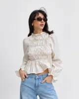 Remera color crema con diseño fruncido en el cuerpo, cuello alto con volados y mangas largas abullonadas con puños elastizados.