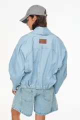 Chaqueta corta de jean color crudo, de silueta holgada, con mangas ranglan, solapas anchas y detalles de costuras pespunteadas a contratono.
