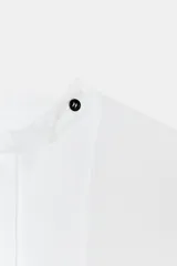 Camisa amplia de algodón con cuello redondo, manga por debajo del codo con puño y bajo asimétrico con aberturas laterales. Presenta cierre frontal con botones ocultos por solapa.