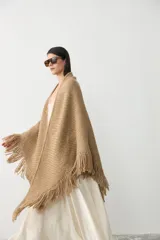 Ruana tejida en lana merino extrafina con lino y viscosa, de diseño triangular con textura en relieve y flecos en los bordes. Pieza versátil de calce holgado y envolvente.