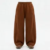 Pantalón de corte baggy y silueta oversize, color marrón chocolate, confeccionado en tejido de algodón. Presenta cintura elástica, bolsillos laterales y costuras decorativas verticales que estructuran el diseño.