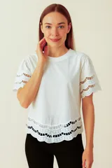 Remera blanca de manga corta con cuello redondo, calce holgado y detalles de broderie calado en forma de ondas en las mangas y el ruedo inferior.