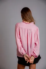 Camisa de color celeste con volados decorativos en el cuello y la parte delantera, cuenta con cordones para ajustar el escote, mangas largas con puños y corte holgado.