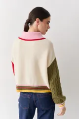 Cardigan de punto con diseño color block, cuerpo en color crema, cuello polo rosado con borde rojo, manga derecha verde oliva y manga izquierda roja. Presenta mangas con tejido de ochos, puños acanalados multicolor y cierre frontal con botones.