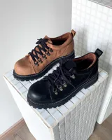 Zapatos tipo borceguíes bajos de cuero vacuno color tostado, con suela track negra de goma y cordones negros con ganchos metálicos.