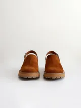 Zueco de cuero gamuzado color óxido, con tira trasera ajustable mediante hebilla metálica. Presenta una suela de plataforma con textura acanalada y detalle de textura reptil en la tira posterior.