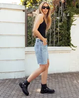 Bota de caña alta confeccionada en cuero negro, con suela track de goma. Presenta un diseño versátil con dos hebillas ajustables en la parte superior de la caña y una correa decorativa con tachas metálicas y argollas en la zona del tobillo.