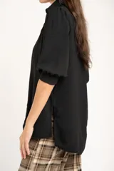 Blusa de corte oversize en color blanco, con cuello camisero, cierre frontal de botones y mangas tres cuartos con sutiles frunces en los hombros.