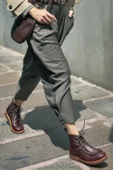 Bota de cuero vacuno color bordó con acabado charol, diseño de caña media con cordones y ganchos metálicos. Presenta costuras visibles en la puntera y suela de goma tipo crepe.
