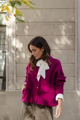 Chaqueta de lana afieltrada color amarillo, con cuello camisero, cierre frontal con broches a presión y bolsillos delanteros. Presenta un diseño de corte holgado con una apertura en la espalda que aporta movimiento.