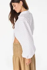 Top blanco de manga larga con diseño abullonado, cuello camisero, cierre frontal con botones y nudo ajustable en la cintura. Con textura sutil en la tela.