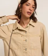 Campera color beige confeccionada en sarga de algodón, de corte regular, con cuello camisero, cierre abotonado, manga larga, bolsillos frontales y recortes.