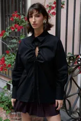 Camisa oversize de manga larga en color blanco, confeccionada en algodón. Presenta cuello clásico, puños abotonados y una abertura central ovalada con jaretas ajustables que permiten fruncir la prenda.