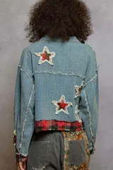 Campera de jean con textura acanalada, cierre frontal y diseño con apliques de estrellas desgastadas. Presenta detalles de tela escocesa en los puños y el ruedo, con bordes desflecados y bolsillos frontales con solapa.