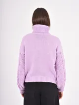 Polera de tejido de punto color lila, con cuello alto doblado y diseño de trenzas en el frente y las mangas. Presenta puños y ruedo acanalados.