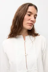 Blusa de manga larga color marrón con cuello redondo y cierre frontal con alamares. Presenta costuras visibles y diseño estructurado.