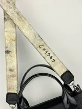 Cartera marrón de cuero genuino con doble asa corta y correa bandolera estampada con la frase "Chabas, soy real, no perfecta".