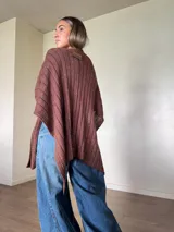 Ruana tejida de algodón con hilo lurex en punto jersey, color azul, con diseño amplio y detalle de etiqueta de cuerina en la parte posterior.