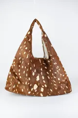 Cartera de cuero vacuno con pelo en diseño animal print similar a piel de ciervo, silueta triangular y asa integrada.