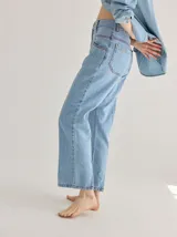 Jean de corte recto confeccionado en denim azul oscuro, con costuras a la vista en color rojo contrastante. Presenta un diseño de tiro alto con bolsillos frontales y cierre de botón.