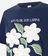 Remera de algodón color blanco, con cuello redondo y manga corta. Presenta un estampado con la frase 'Soy flor. Soy latina' y flores bordadas en relieve con textura tejida.