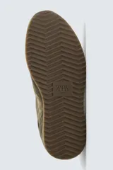 Zapatilla deportiva de estilo casual, confeccionada en una combinación de piezas de cuero con acabado de gamuza y paneles textiles. Presenta una horma redonda, cierre mediante cordones y una suela dentada en tono contrastante.