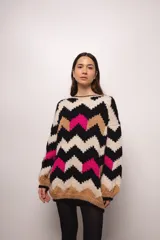 Buzo tejido a mano en lana merino, con diseño de patrón en zigzag multicolor en tonos crema, negro, azul y tostado. Presenta un corte holgado, cuello redondo y mangas largas con puños acanalados.