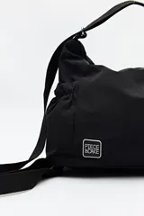 Cartera tipo hobo de nylon color negro, con diseño soft, correa regulable y parche con logo de la marca Piece of Cake.