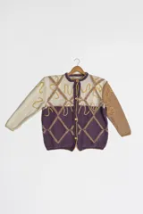 Cárdigan tejido a mano con lana merino y seda natural, con silueta holgada, manga caída y escote clásico. Presenta bordados artesanales y cierre frontal con botones. Tiene un diseño geométrico con rombos en color lila y beige, y detalles bordados en dorado.