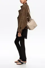 Bolso shopper mediano de nylon color beige con estructura blanda, doble asa corta de mano y correa fina ajustable. Cuenta con cierre de botón a presión, bolsillo interior con cierre y aplique metálico con el logo de la marca en el frente.