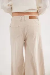 Pantalón sastrero de tiro medio confeccionado en pana de algodón. Presenta un diseño de pierna ancha con costuras verticales decorativas, bolsillos delanteros y traseros, y un detalle de aplique con ojalillo metálico en el ruedo de una de las piernas.