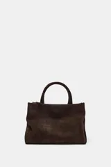 Bolso de mano formato city confeccionado en gamuza color marrón oscuro. Cuenta con doble asa de mano, asa bandolera extraíble, compartimento interior con cierre y bolsillo exterior con imán.