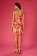 Vestido corto con estampado tropical en tonos rosados, amarillos y naranjas. Tiene breteles finos, escote en V y abertura en la cintura.