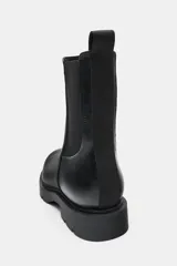 Botín Chelsea de caña media en color negro, con paneles elásticos laterales y tirador trasero. Presenta punta redonda y suela track robusta de 3 cm de altura.