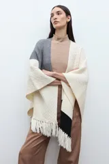 Ruana de tejido de punto con diseño color block en tonos crudo, gris y negro, con terminación de flecos en el ruedo y textura en relieve.