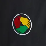 Remera de algodón negra con cuello redondo y mangas cortas. Presenta el logo del trébol de Adidas bordado en blanco en el lado derecho del pecho y un parche circular con los colores rasta en el lado izquierdo. Incluye un parche rectangular en la parte inferior con la inscripción Football is Freedom y una imagen de Bob Marley.